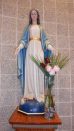 Statue of the Blessed Mother with a tall glass vase filled with two small palm fronds & five roses--- 2 red, 3 pink--- beside her left foot