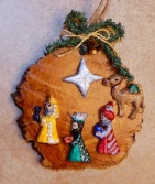 Painted wood ornament of the Magi and a camel guided by the Star & greenery with a tiny gold-colored bell and cord at the top.
