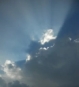 Sun rays emanating from dark-blue clouds in a blue sky with white clouds